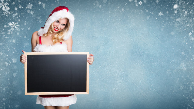 Weihnachtsfrau mit leerer Kreidetafel für eigene Nachricht vor Winterlandschaft 
