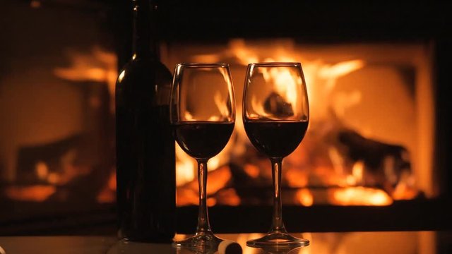 Bottle and two red wine  wineglasses over fireplace background.