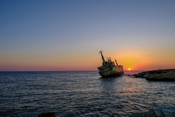 Sunset of shipwreck listing by rocks in the sea near Pafos, Cyprus.