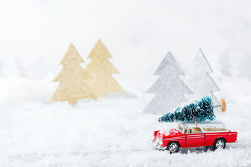 Toy car carrying christmas tree in a snow forest