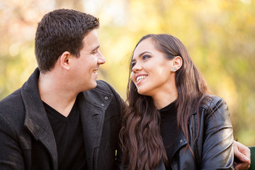 Close up of beautiful in love couple sitting on a bench in autumn park