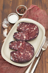 smoked sausage morcela on white dish on wooden background