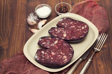 smoked sausage morcela on white dish on wooden background