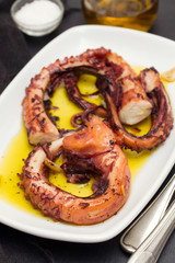 grilled octopus with garlic on white dish on wooden background