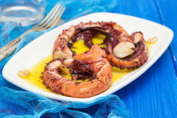 grilled octopus with garlic on white dish on wooden background