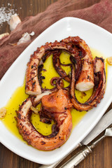 grilled octopus with garlic on white dish on wooden background