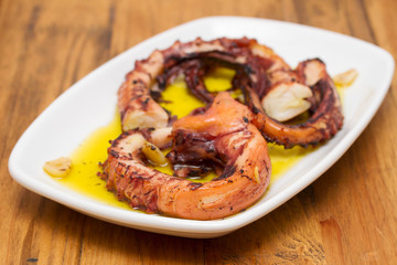 grilled octopus with garlic on white dish on wooden background