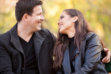 Fototapeta premium Close up of happy beautiful in love couple sitting on a bench in autumn park