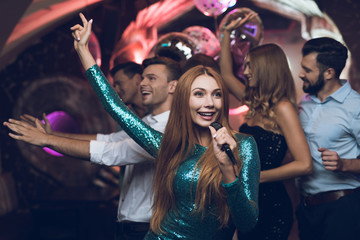 A woman in a green dress is singing songs with her friends at a karaoke club. Her friends have fun...