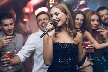 A woman in a black dress is singing songs with her friends at a karaoke club. Her friends have fun...