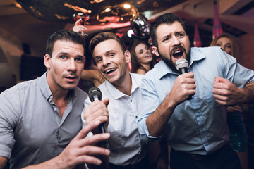 Three men sing at a karaoke club. Young people have fun in a nightclub. They are very cheerful and...