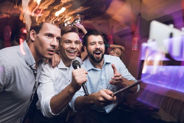Three men sing at a karaoke club. Young people have fun in a nightclub. They are very cheerful and they smile.