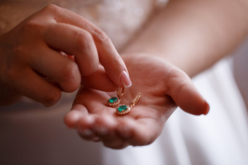 Bride keeps earrings with green precious stones