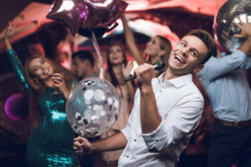 Young people have fun in a nightclub and sing in karaoke. In the foreground is a man in a white...