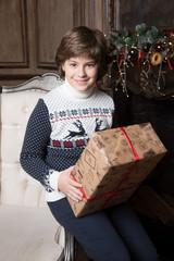 A young boy with a box with a Christmas gift is smiling. Concept of Christmas magic evening at home, decorations, the best time to make a wish, to let all dreams come true in the eve of Christmas.