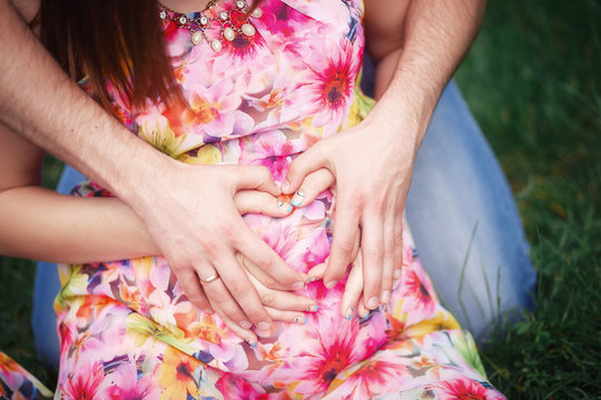 husband hugging his pregnant wife in a bright dress