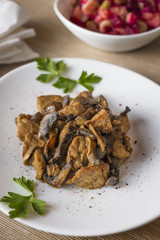 Pork bites with mushrooms in a white plate decorated with parsley and potatoes and beetroot salad