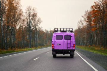 Fototapeta na wymiar A lilac van driving on a road along the forest