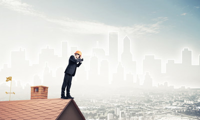 Engineer man standing on roof and looking in binoculars. Mixed m