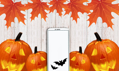 telephone with a white screen, along with yellow leaves and carved pumpkins, lies on a wooden table - 181540660