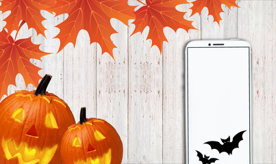 telephone with a white screen, along with yellow leaves and carved pumpkins, lies on a wooden table - 181540858
