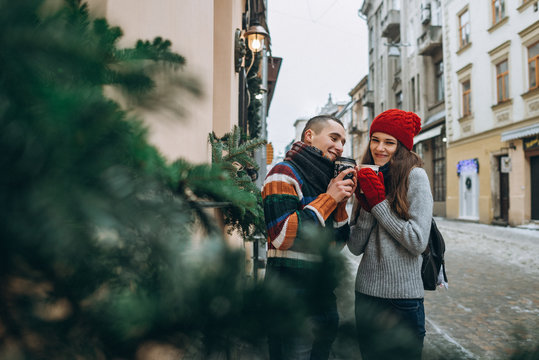 Young loving couple dressed in knitted clothes staying with coffee cups on the street in winter