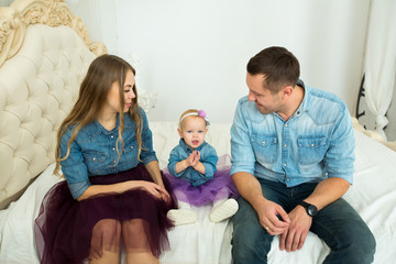 beautiful modern family in jeans attire sitting on the bed with little girl daughter