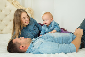 Fototapeta na wymiar beautiful modern family in denim dress lying on the bed with a little girl daughter