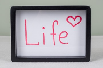 Text word life, in black frame, on white table.