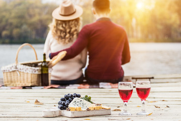 Romantic dinner outdoors. Glasses with red wine, grapes and cheese on wooden board. Young couple...