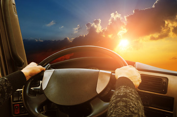 Truck dashboard with driver's hand on the steering wheel against night sky with sunset