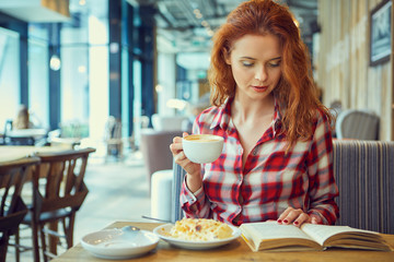 Red haired woman reading book  in cafe. City break  concept
