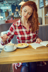 Red haired woman reading book  in cafe. City break  concept