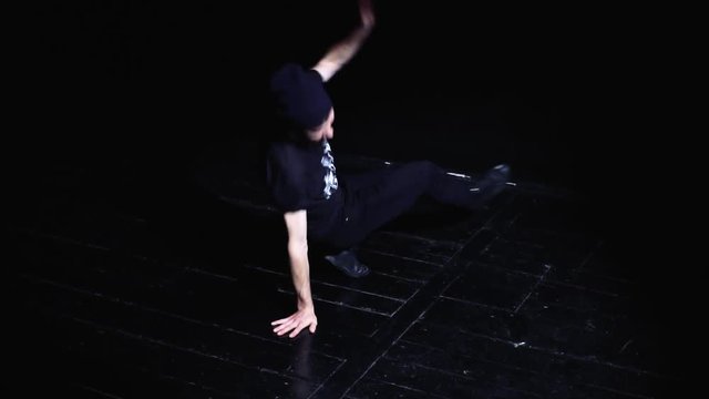 Street dancer breakdance on a black wooden floor in a black studio