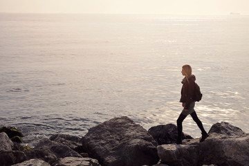 Obraz premium Young woman walking alone on stone sea coast. My dream, my goal , my way concept