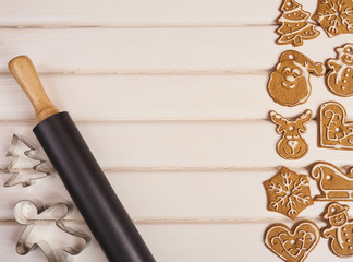 Christmas cookies, rolling pin and cookie cutters on the white wooden background.