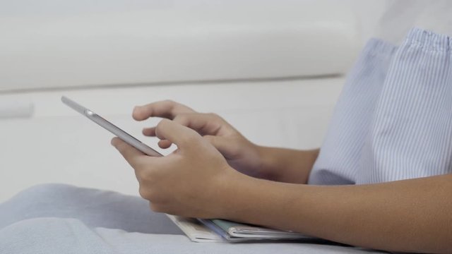 Cute girl sitting on sofa with tablet computer doing homework and playing games