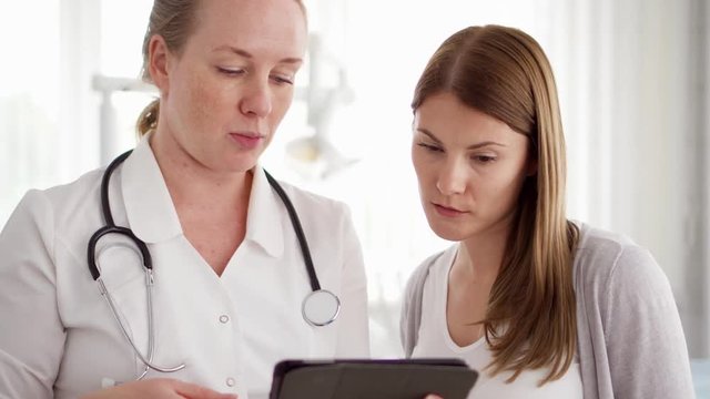 Female professional doctor at work. Woman physician with stethoscope consulting patient in modern clinic. Showing something on tablet