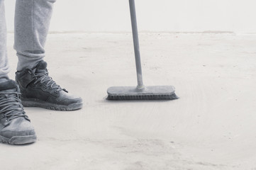 people, housework, cleaning and housekeeping concept - close up of legs with broom sweeping floor