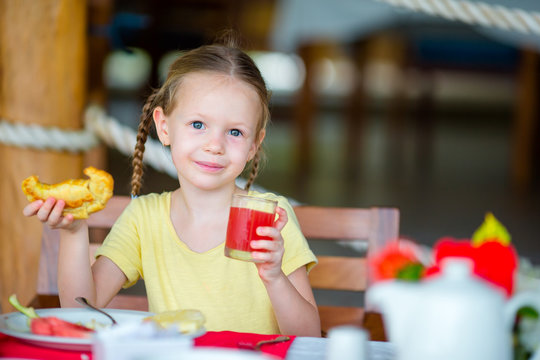 Adorable little girl having breakfast at outdoor cafe