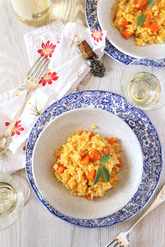 Two plates of pumpkin risotto and glass of white wine 