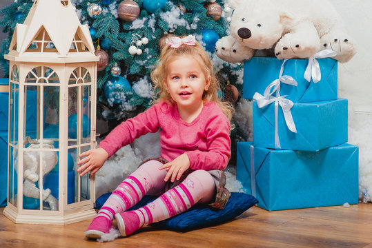 Blonde little girl sitting and smiling nearly decorated christmas tree 