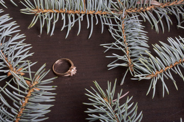 On the surface of the table is a golden ring. Around there are branches of blue spruce.