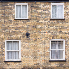 Facade of a Victorian house residential building with four Victorian windows with white wooden sash and white curtains on a restored brick wall