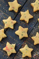 Overhead view of homemade Xmas star sugar cookies with colorful sprinkles on festive blue wooden background