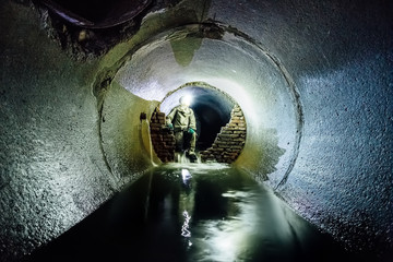 Sewer tunnel worker in special chemical protective suite in underground sewer tunnel examining...