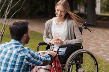 Obraz premium Woman in a wheelchair in the park with a man. A man covers her legs with a blanket.