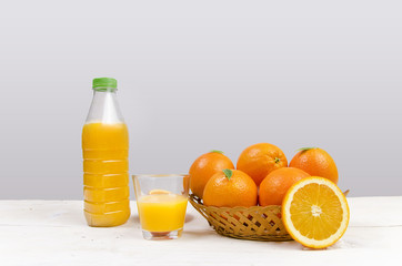 Bottle of orange juice, next to glass and bowl full of oranges. Copy space