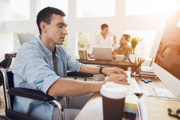 Disabled person in the wheelchair works in the office at the computer.