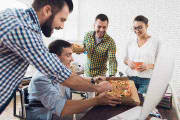 Office workers and man in a wheelchair are eating pizza. They work in a bright and modern office.
